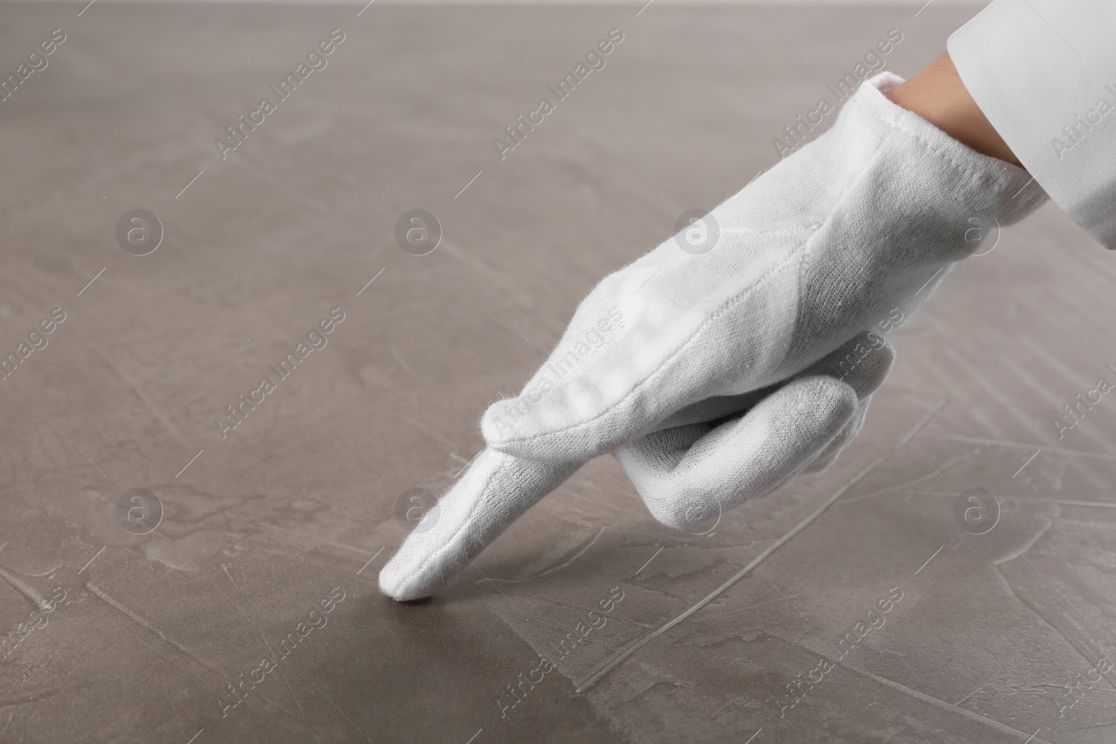 Photo of Person in white glove checking cleanliness of beige stone table, closeup
