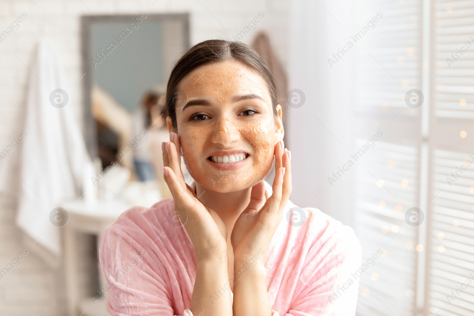 Photo of Young woman applying natural scrub on face in bathroom