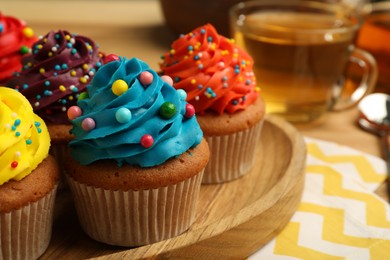 Photo of Delicious cupcakes with colorful cream and sprinkles on wooden board, closeup