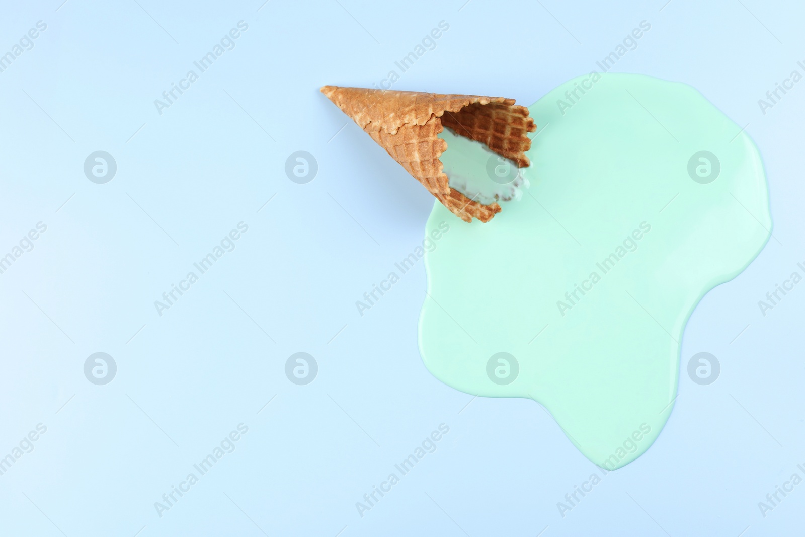 Photo of Melted ice cream and wafer cone on light blue background, top view. Space for text