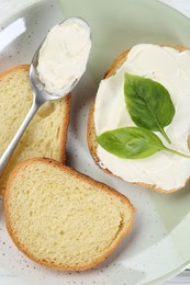 Photo of Pieces of bread with cream cheese and basil leaves on white wooden table, top view