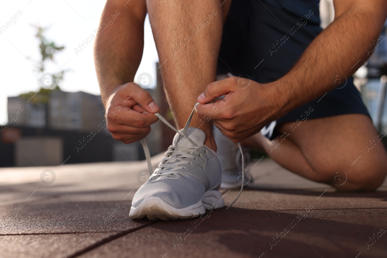 Photo of Man tying shoelaces before running outdoors on sunny day, closeup