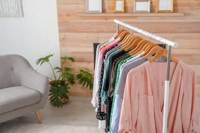 Wardrobe rack with stylish clothes and sofa in dressing room. Space for text