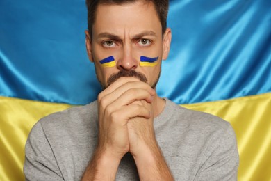 Man with clasped hands near Ukrainian flag, closeup
