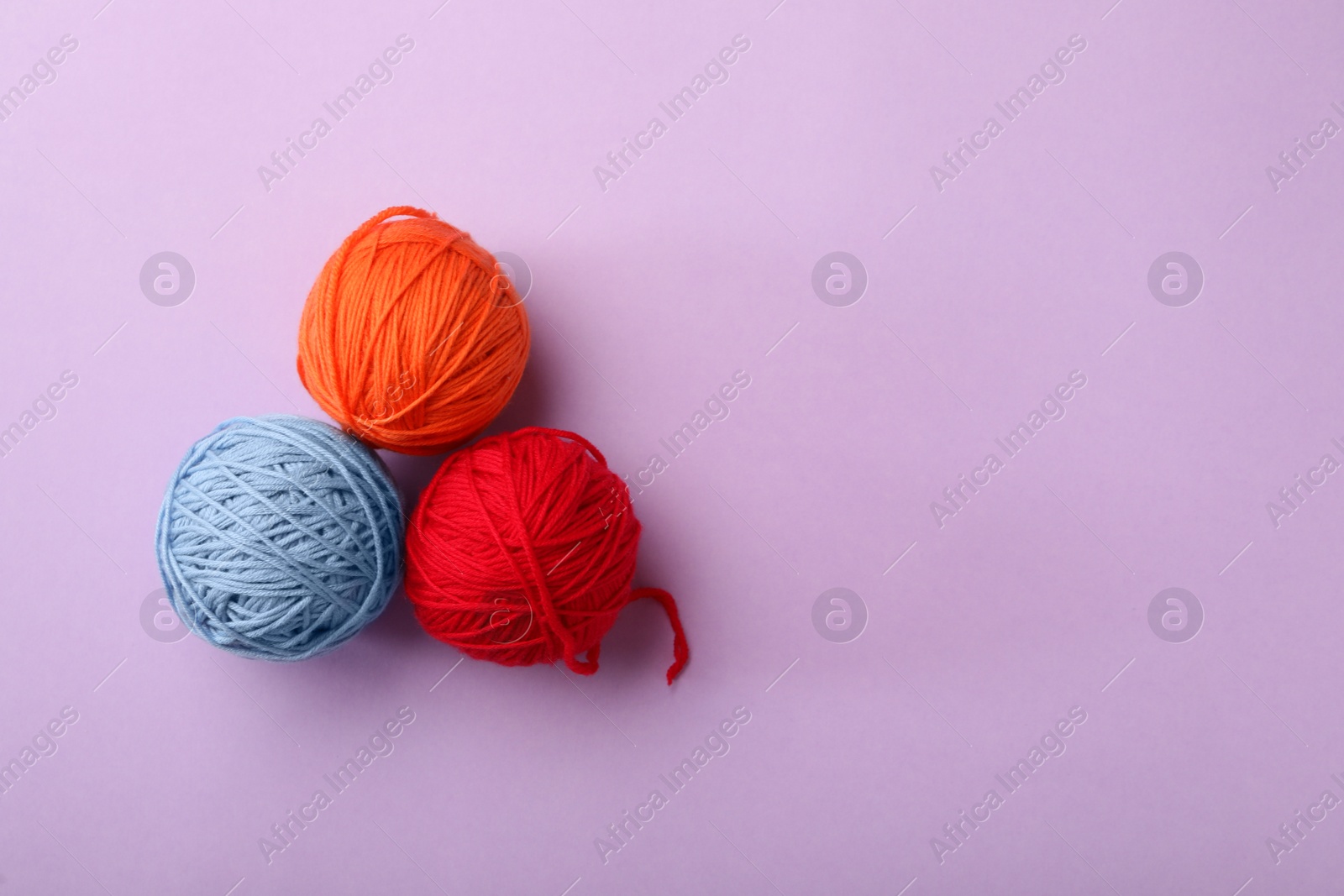 Photo of Soft colorful woolen yarns on lilac background, flat lay. Space for text