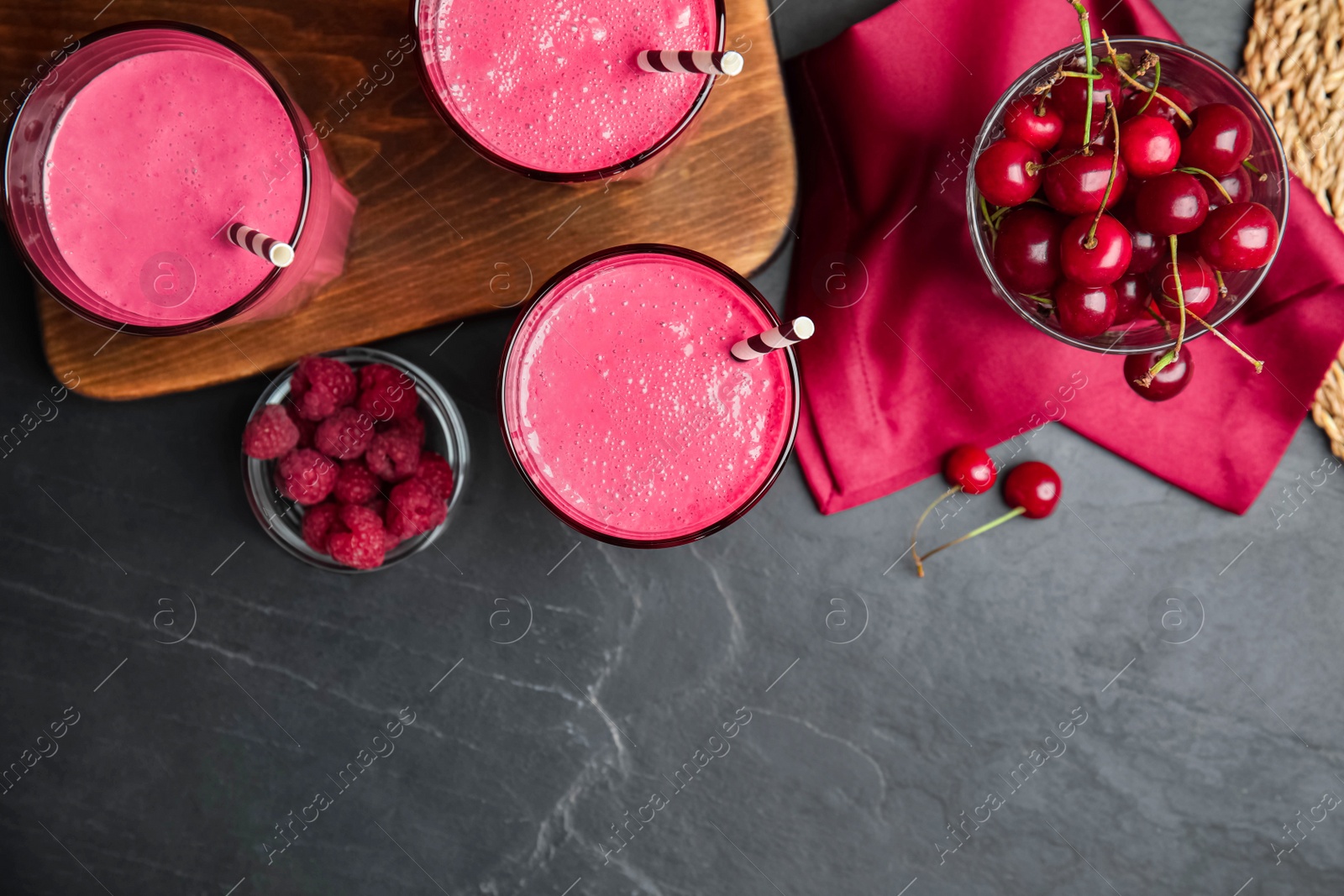 Photo of Tasty fresh milk shakes with berries on black table, flat lay. Space for text