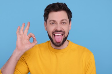 Happy man showing his tongue and making ok gesture on light blue background