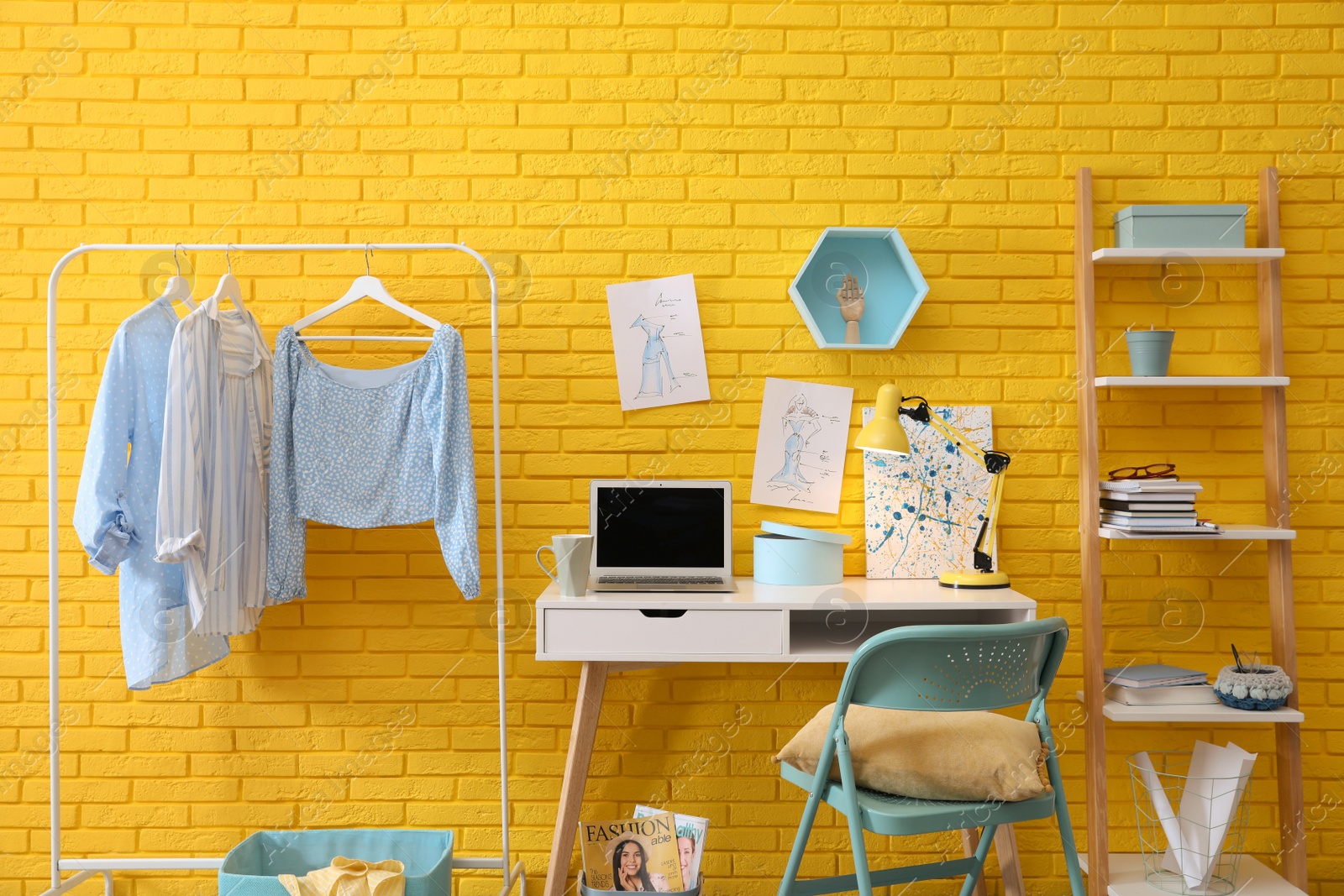 Photo of Fashion designer's workplace with wooden furniture and laptop near yellow brick wall. Stylish interior