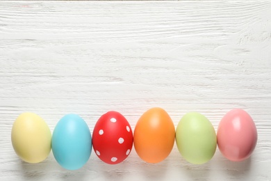 Flat lay composition of colorful painted Easter eggs on wooden table, space for text