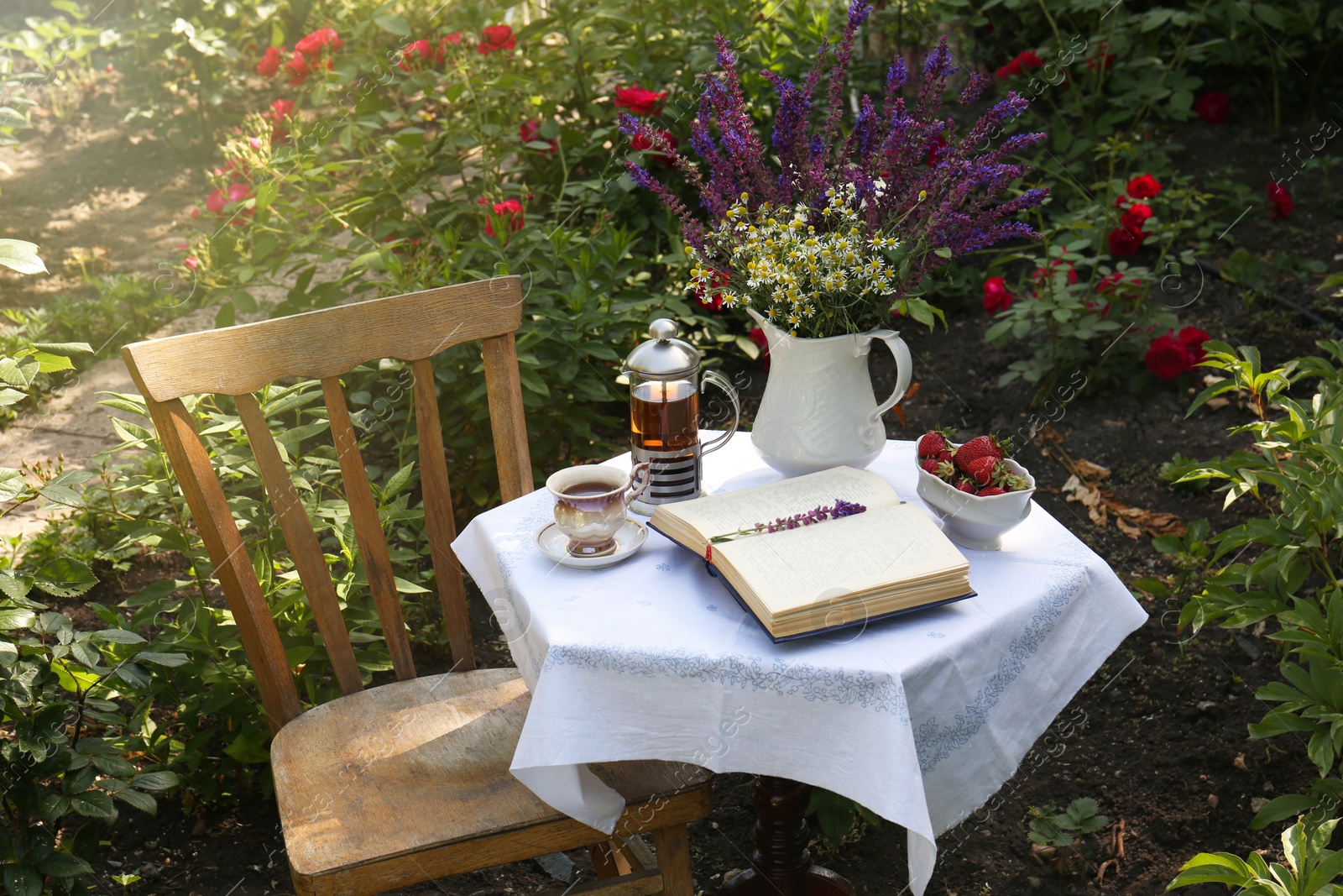 Photo of Beautiful bouquet of wildflowers and books on table served for tea drinking in garden