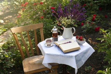 Photo of Beautiful bouquet of wildflowers and books on table served for tea drinking in garden