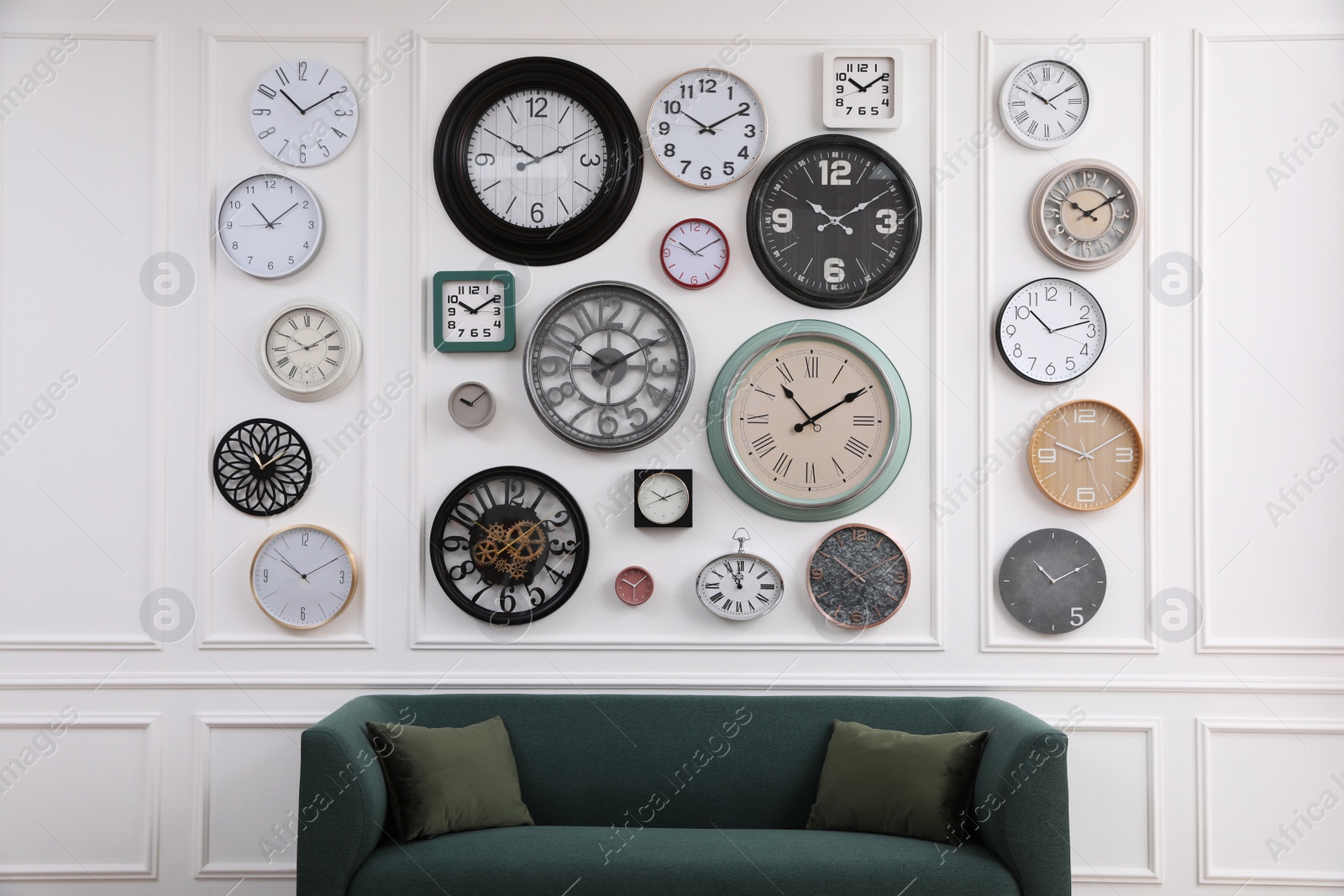 Photo of Collection of different clocks and comfortable sofa in stylish room. Interior design