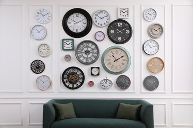 Photo of Collection of different clocks and comfortable sofa in stylish room. Interior design