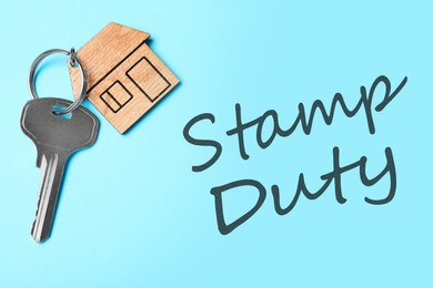 Image of Stamp duty. Key with trinket in shape of house on light blue background, top view