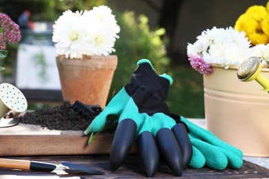 Photo of Gardening gloves and different flowers on table outdoors