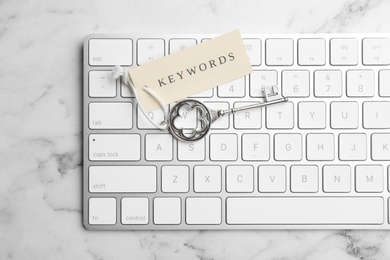 Photo of Keyboard, vintage key and tag with word KEYWORDS on white marble table, top view