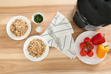 Photo of Delicious rice with vegetables served on wooden table, flat lay. Multi cooker recipes