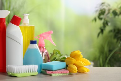 Photo of Spring cleaning. Detergents, supplies and beautiful flowers on wooden table outdoors, space for text