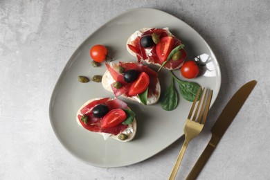 Photo of Delicious sandwiches with bresaola, cream cheese, olives and tomato served on light table, top view