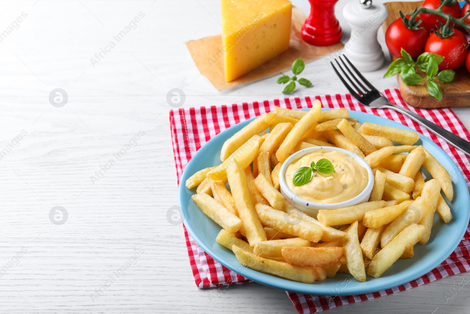 Photo of Delicious French fries and cheese sauce with basil on white wooden table, space for text