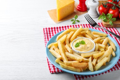 Photo of Delicious French fries and cheese sauce with basil on white wooden table, space for text