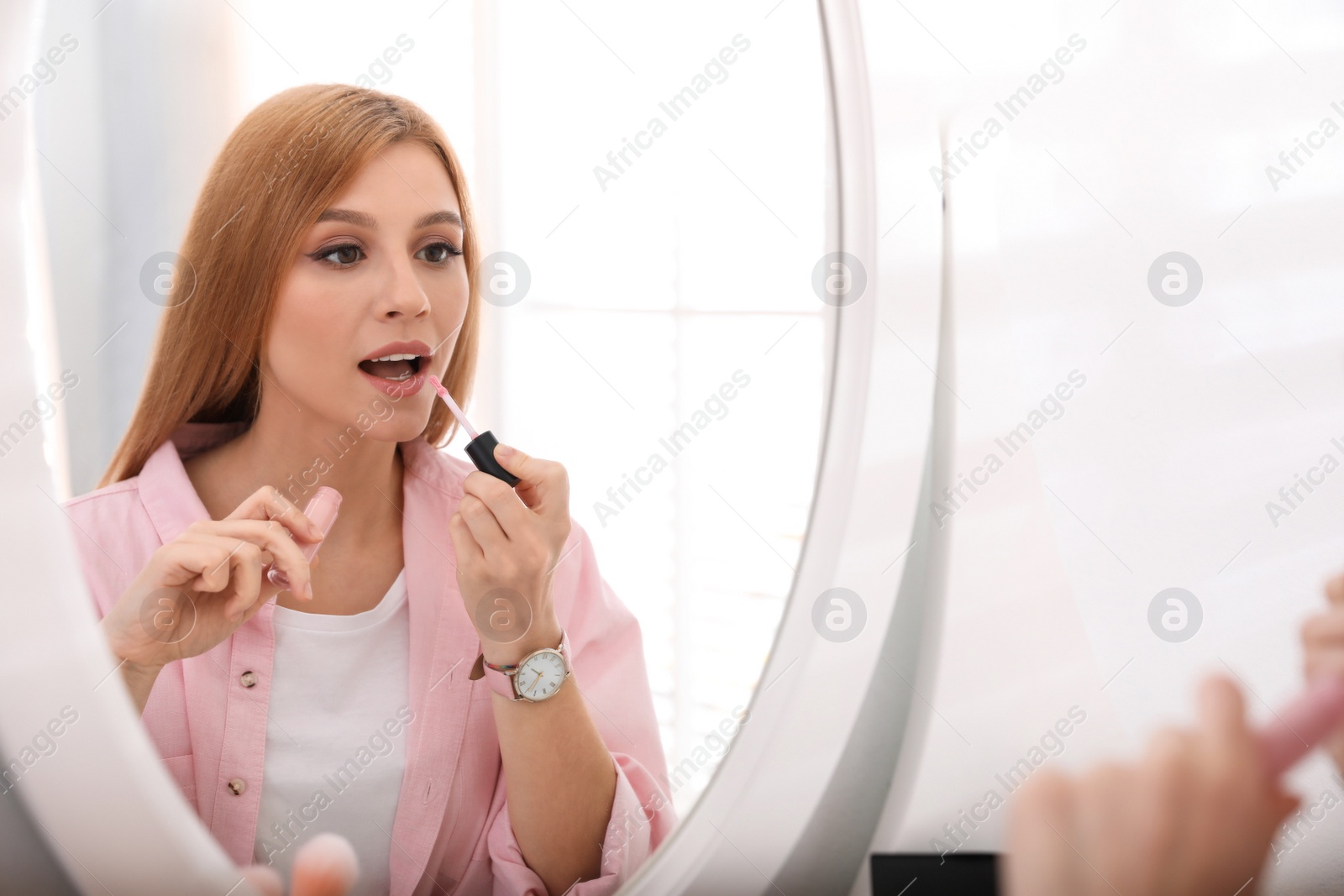 Photo of Beautiful young woman applying makeup near mirror indoors