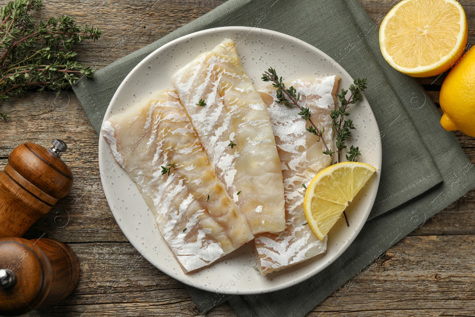 Photo of Fresh raw cod fillets with thyme and lemon on wooden table, flat lay