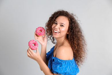 Photo of Beautiful African-American woman with donuts on light grey background