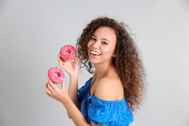 Beautiful African-American woman with donuts on light grey background