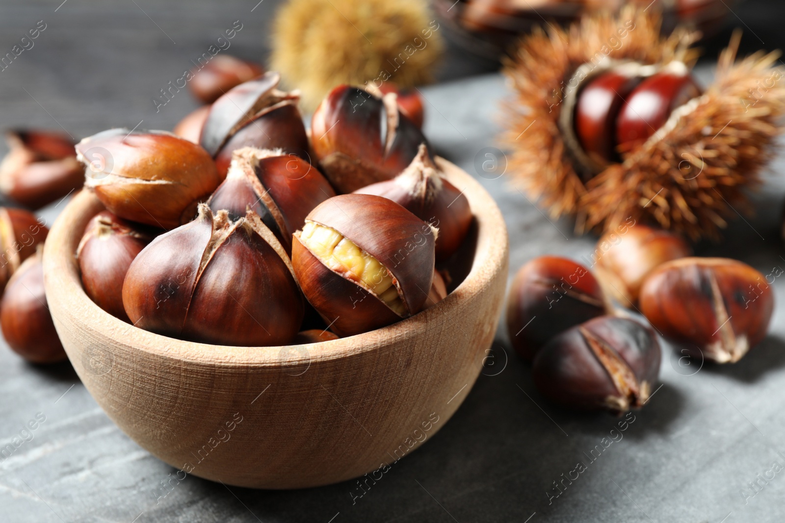 Photo of Delicious roasted edible chestnuts in wooden bowl on grey marble board, closeup