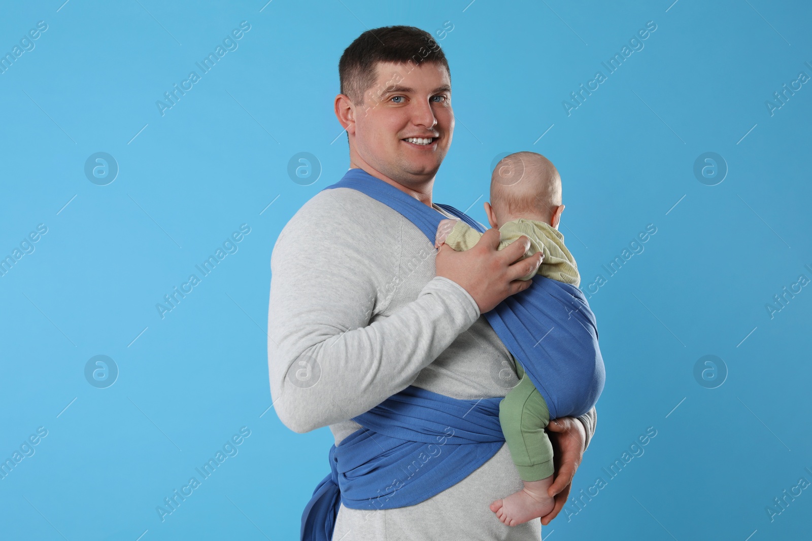 Photo of Father holding his child in sling (baby carrier) on light blue background