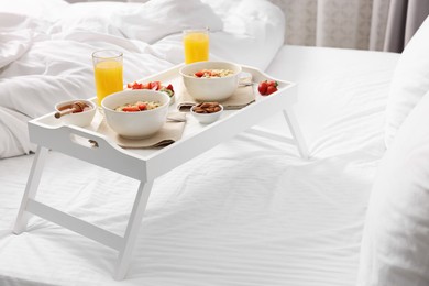 Photo of Tasty breakfast served in bed. Oatmeal, juice, fruits, almonds and honey on tray, space for text