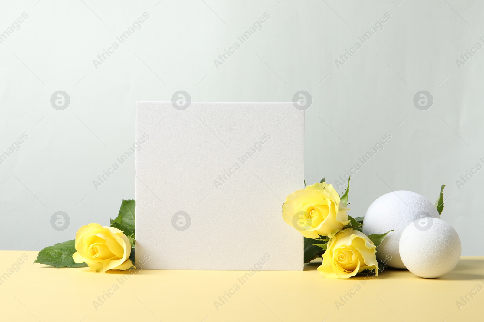 Photo of Beautiful presentation for product. Geometric figures and yellow roses on beige table against light grey background, space for text