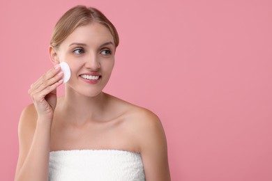 Photo of Young woman cleaning her face with cotton pad on pink background. Space for text