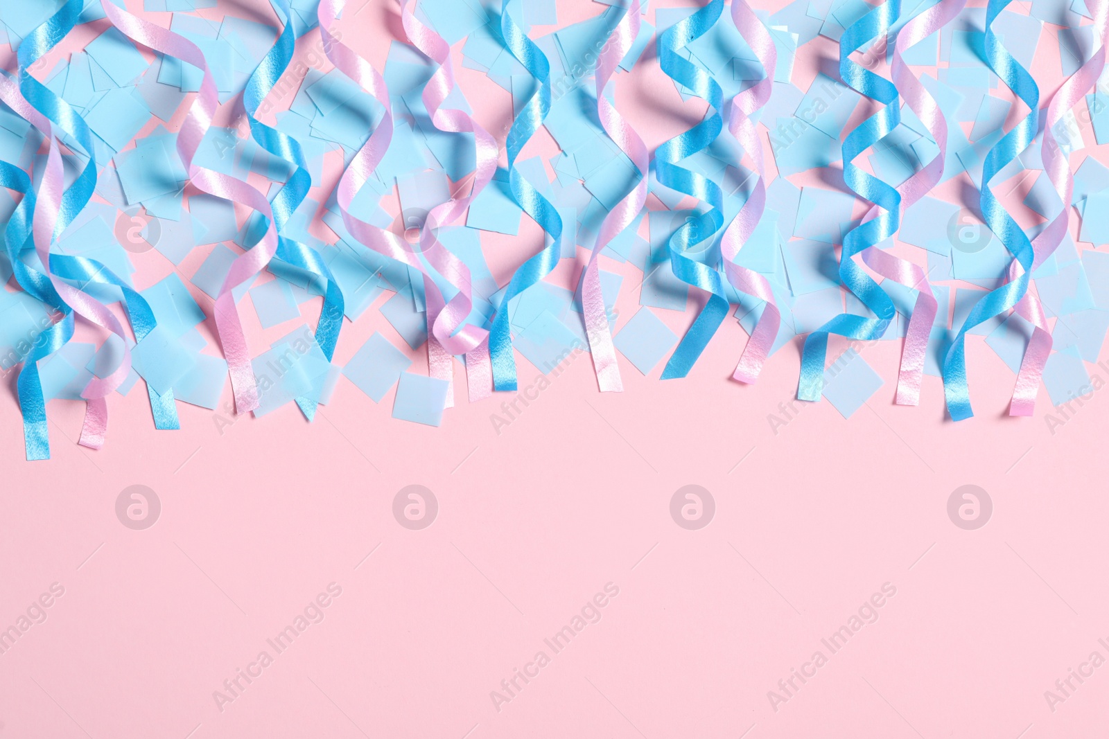 Photo of Shiny serpentine streamers and blue confetti on pink background, flat lay. Space for text
