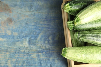Photo of Wooden crate with fresh ripe green zucchinis on blue table, top view. Space for text