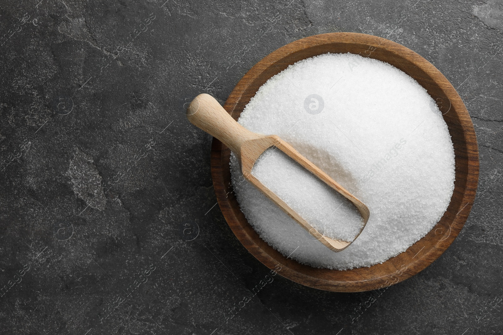 Photo of Granulated sugar in bowl and scoop on grey textured table, top view. Space for text