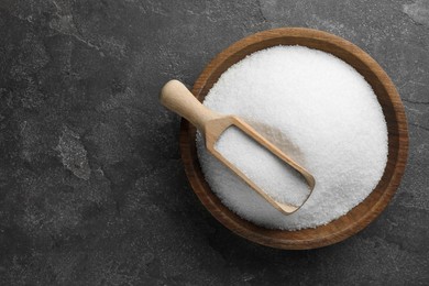 Granulated sugar in bowl and scoop on grey textured table, top view. Space for text