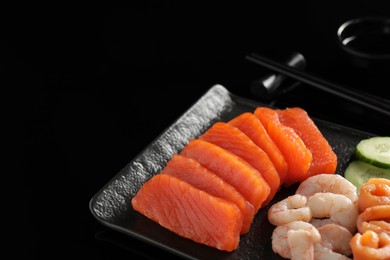 Photo of Delicious sashimi set of salmon and shrimps served with cucumbers on black mirror surface, closeup. Space for text