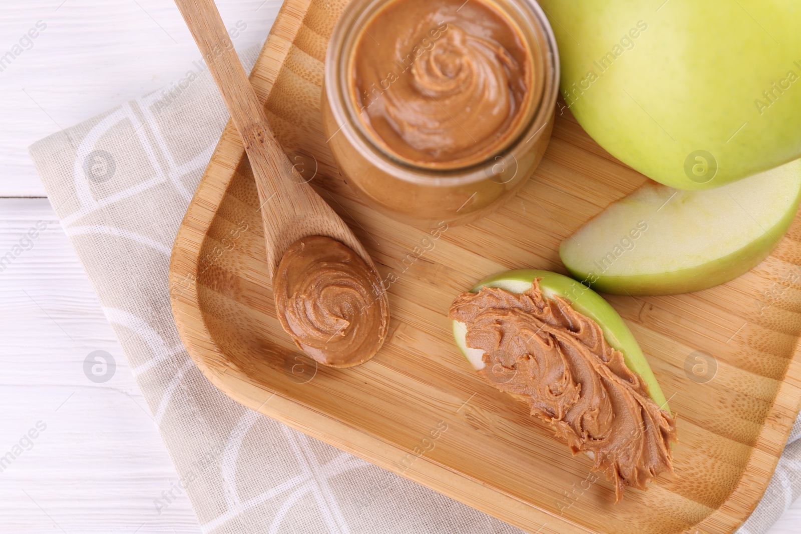 Photo of Fresh green apples with peanut butter on white wooden table, top view