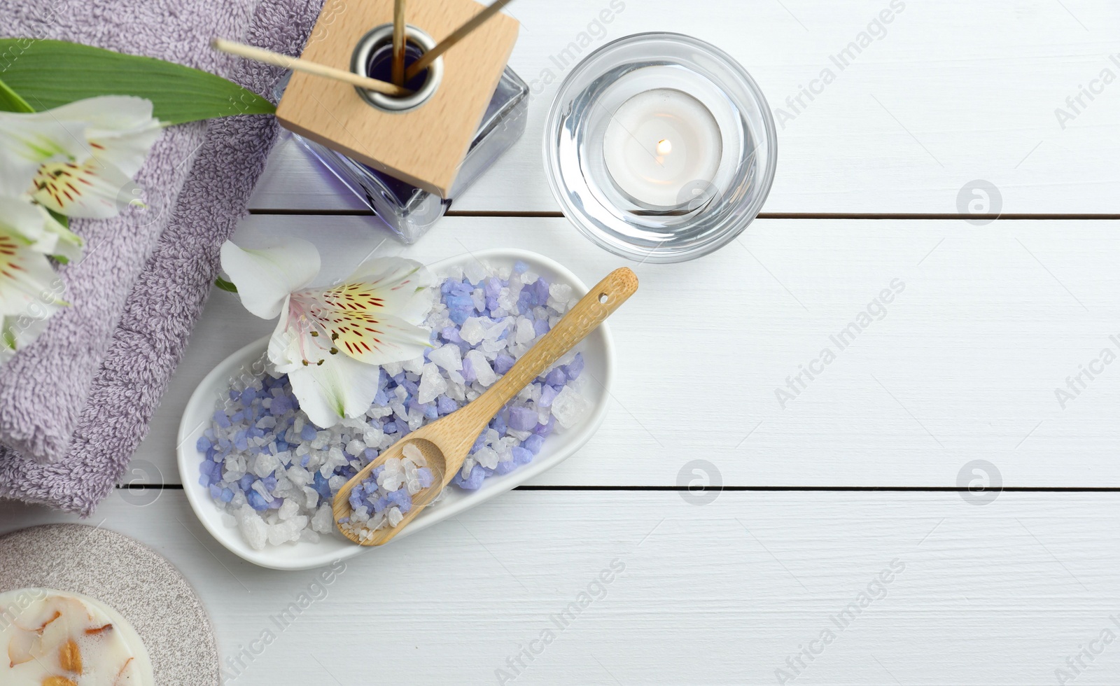 Photo of Spa composition. Towels, reed air freshener, burning candle, sea salt and beautiful flowers on white wooden table, flat lay. Space for text