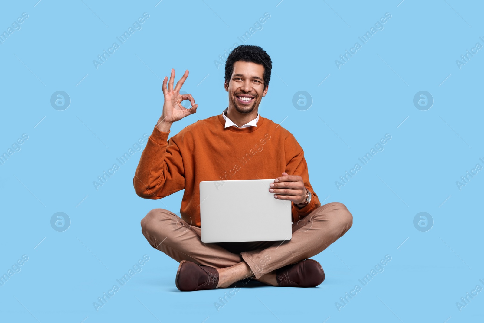 Photo of Handsome man with laptop showing ok gesture on light blue background