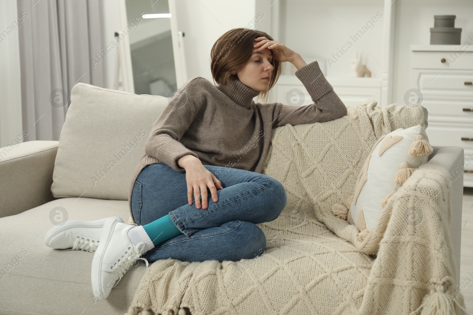 Photo of Sad young woman sitting on sofa at home