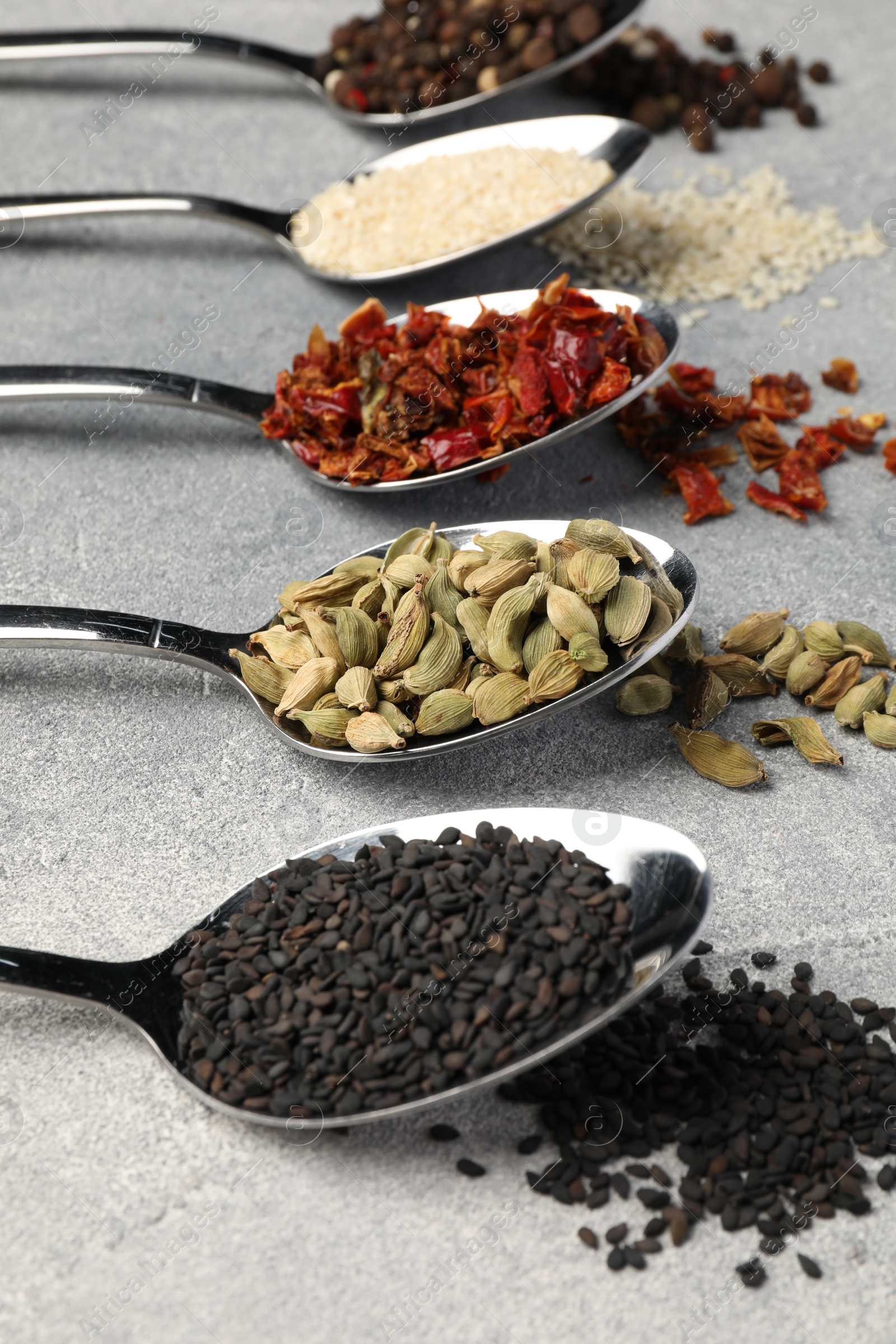 Photo of Metal spoons with different spices on light grey table, closeup