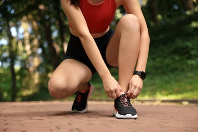 Photo of Woman in sportswear tying shoelaces in park, closeup