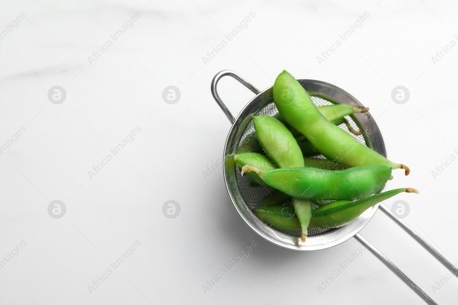 Photo of Sieve with green edamame beans in pods on white table, top view. Space for text