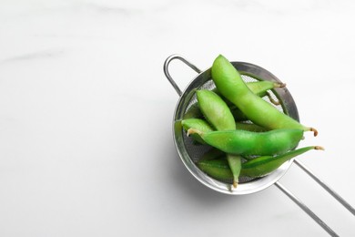 Sieve with green edamame beans in pods on white table, top view. Space for text