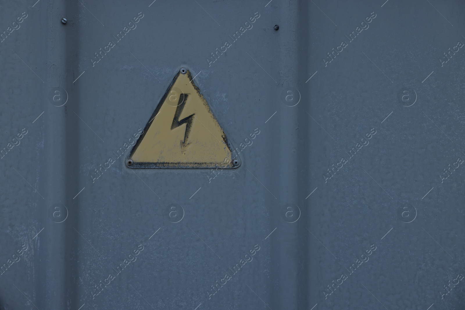 Photo of Yellow high voltage sign on grey metal surface. Space for text