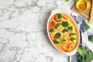 Tasty broccoli casserole in baking dish on white marble table, flat lay. Space for text