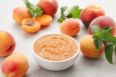 Photo of Apricot puree in bowl and fresh fruits on light grey table